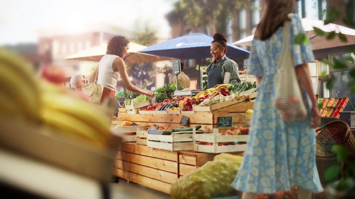 Market-background blurred two women shop at a colorful farmers market stand while two shop purveyors smile and provide service - Orlando farm to table guide companion
