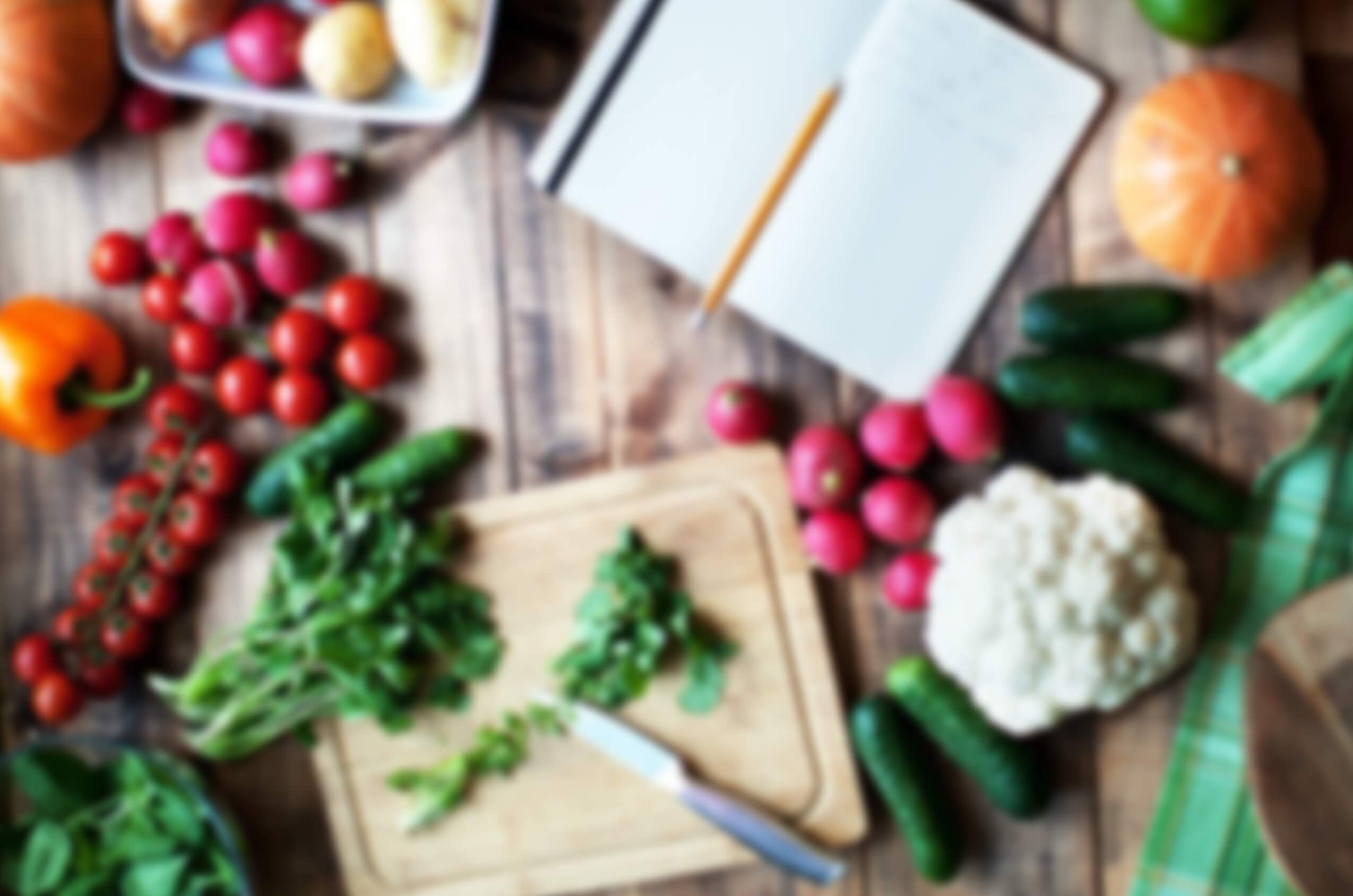 a decorative image of colorful vegetables among a cutting board, knife, and notebook - The Grow Community Cookbook